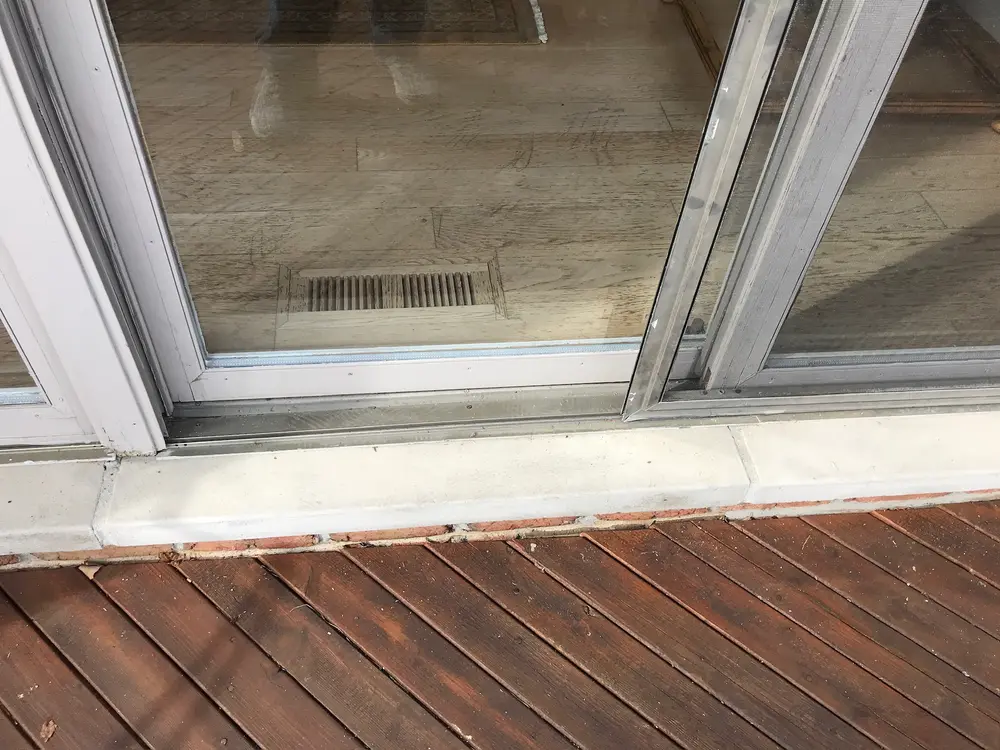 Bottom track and sill of a sliding patio door above a wood deck