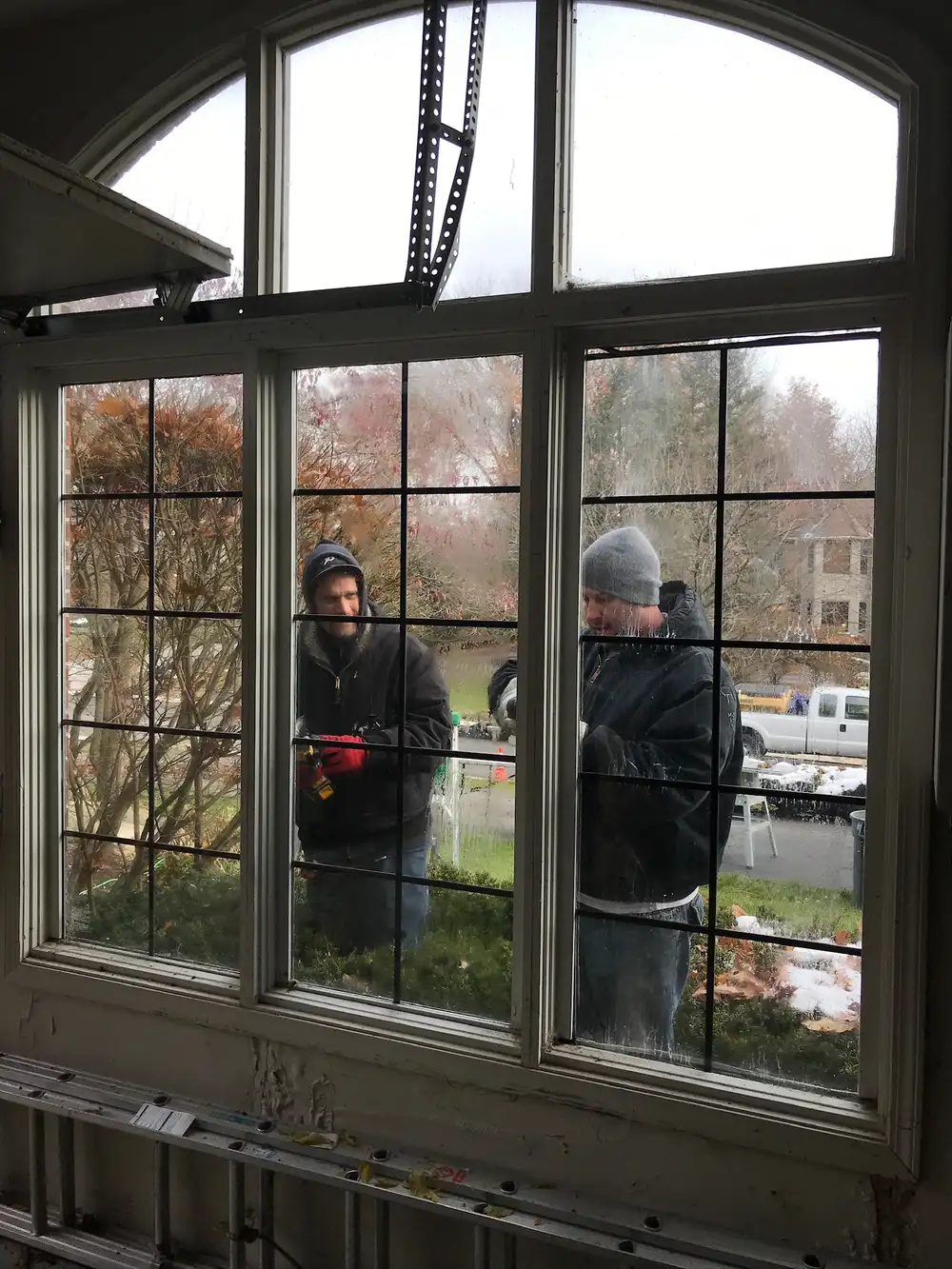 Metro Detroit Window crew working on a large arched window, seen from inside the home